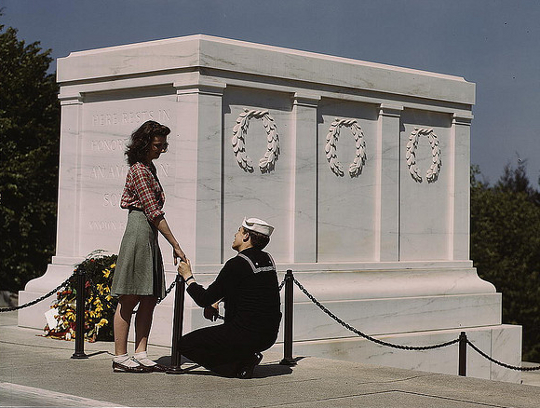 girl wearing a pencil skirt as soldier kneels before her 